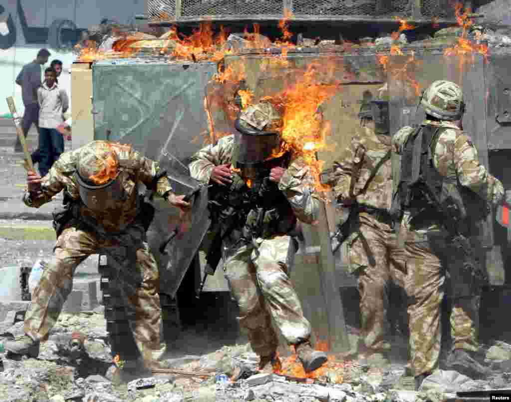 British Army troops are covered in flames from a gas bomb thrown during a protest in Basra, March 22, 2004.