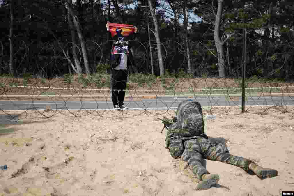 An anti-war activist holds up a sign, "Stop war exercise, Go home," in front of a South Korean marine taking a position during a combined amphibious landing drill of U.S. and South Korea marine corps, in Pohang.
