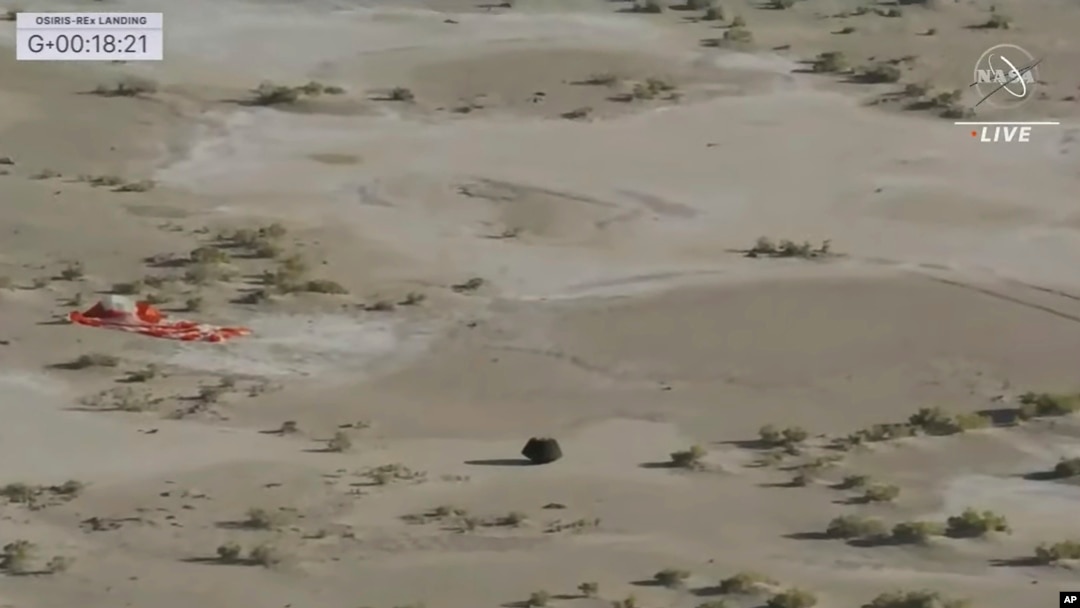 This image taken from video provided by NASA TV shows the capsule released by the Osiris-Rex spacecraft lying on the surface near the parachute after landing to Earth, Sept. 24 2023. (NASA TV via AP)