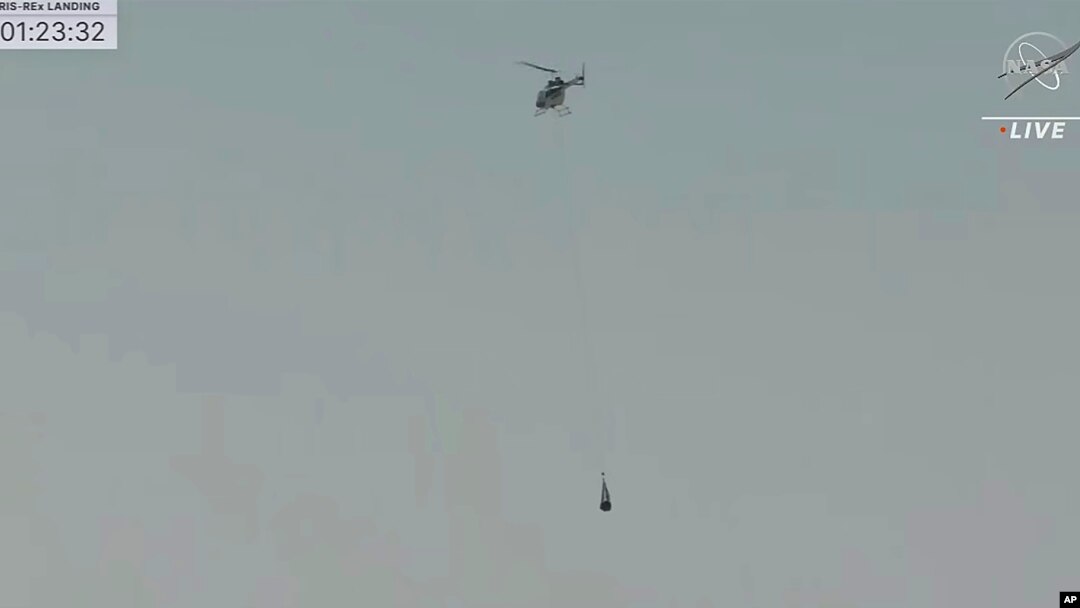 This image taken from video provided by NASA TV shows the capsule released by the Osiris-Rex spacecraft being lifted off by a helicopter after landing to Earth at Dugway Proving Ground, Utah, Sept. 24 2023. (NASA TV via AP)