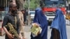 FILE - Afghan burqa-clad women walk past a Taliban security officer along a street in Jalalabad on April 30, 2023. 