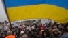 FILE - Ukrainian volunteer Oleksandr Osetynskyi, 44 holds a Ukrainian flag and directs hundreds of refugees after fleeing from the Ukraine arriving at the border crossing in Medyka, Poland, March 7, 2022.
