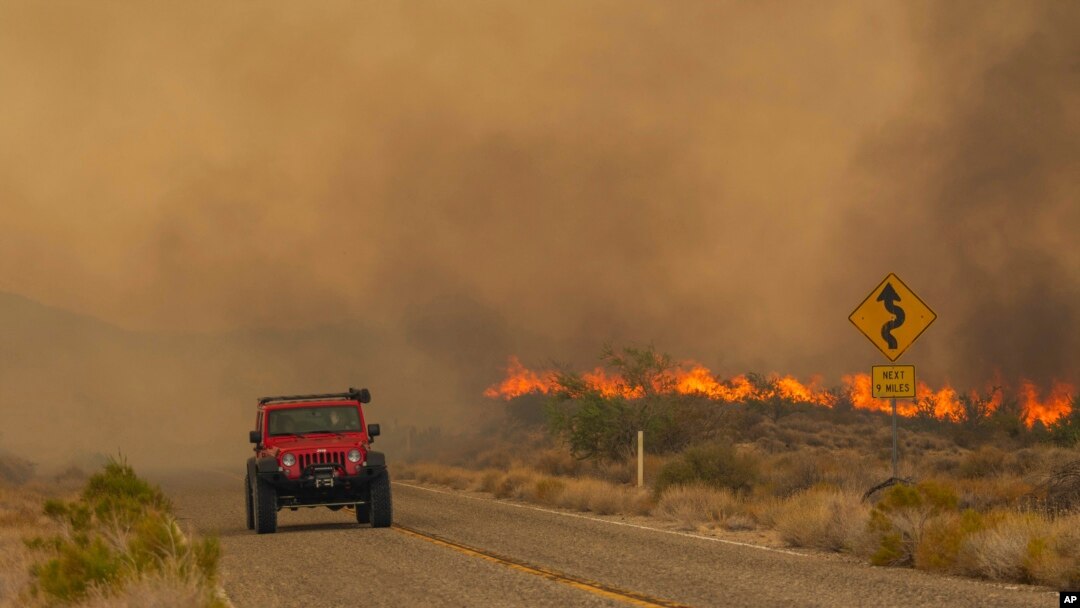 A car passes rising flames from the York Fire in the Mojave National Preserve, California, July 30, 2023.