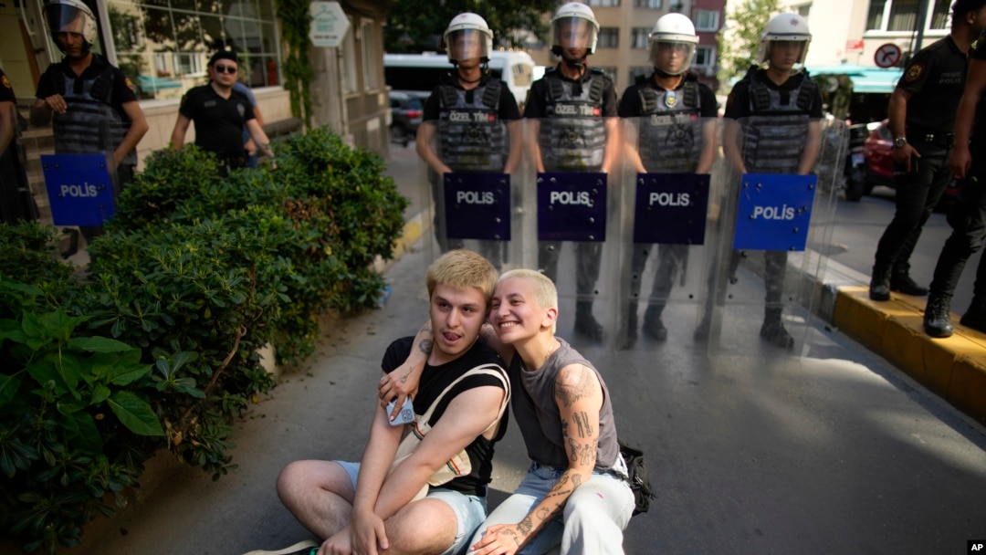 Two people sit next to a line of police officers blocking a street during the LGBTQ Pride March in Istanbul, Turkey, June 25, 2023.
