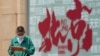 FILE - A boy browses a tablet computer as he walks by a billboard promoting tourism destinations in Beijing on July 19, 2023. China fully reopened to tourists in March, but some statistics show foreign visitors are staying away.