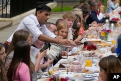 Prime Minister Rishi Sunak hands over a slice of cake to a guest as he attends the Big Lunch party at Downing Street in London, May 7, 2023.