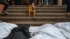 Mourners stand and sit near the shrouded bodies of loved ones killed during the Israeli bombardment of Nasser Hospital in Khan Younis in the southern Gaza Strip, Dec. 27, 2023.