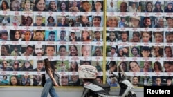 FILE - A woman walks past a wall displaying posters of hostages, most of whom were kidnapped during the deadly Oct. 7 attack by Hamas, in Tel Aviv, Aug. 18, 2024.