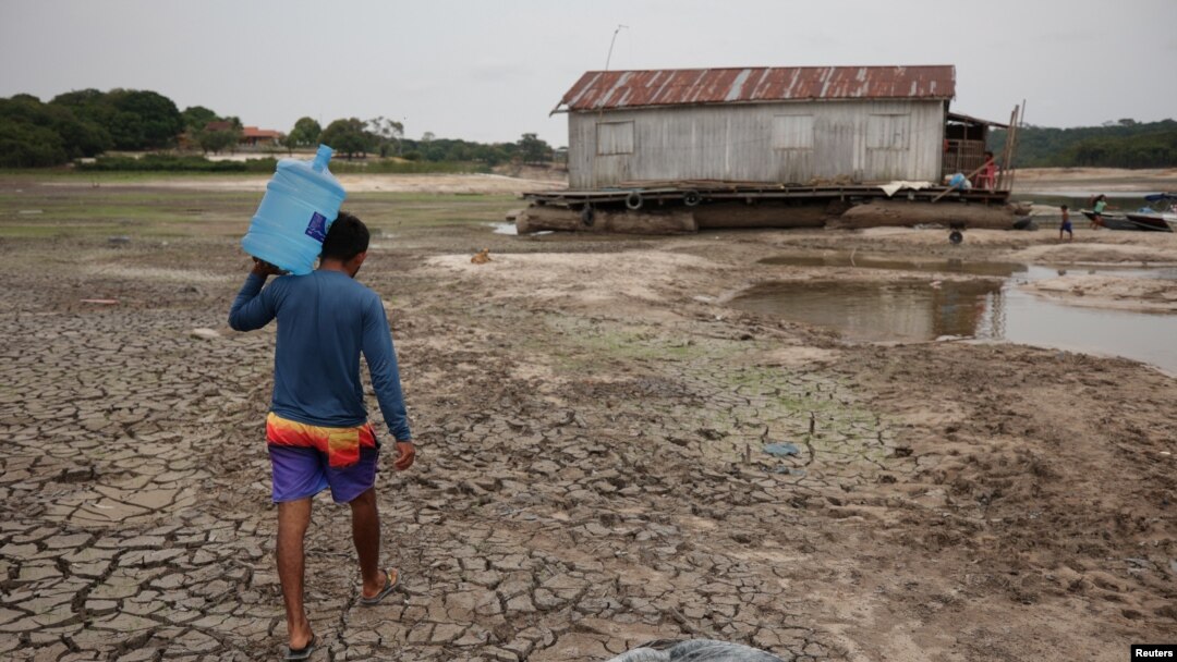 A man carries a bottle of water in a dry area of the Igarape do Taruma stream which flows into the Rio Negro River, in Manaus, Brazil, Oct. 16, 2023. 