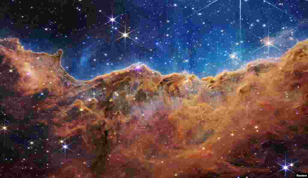 The "Cosmic Cliffs" of the Carina Nebula are seen in an image divided horizontally by an undulating line between a cloudscape forming a nebula along the bottom portion and a comparatively clear upper portion, with data from NASA's James Webb Space Telescope, released July 12, 2022.