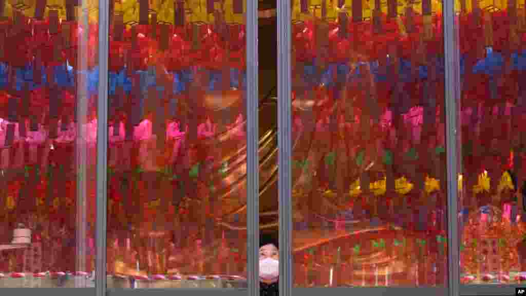 A woman wearing a face mask opens the window which reflects lanterns displayed for upcoming Buddha's birthday celebration at Jogyesa temple in Seoul, South Korea.