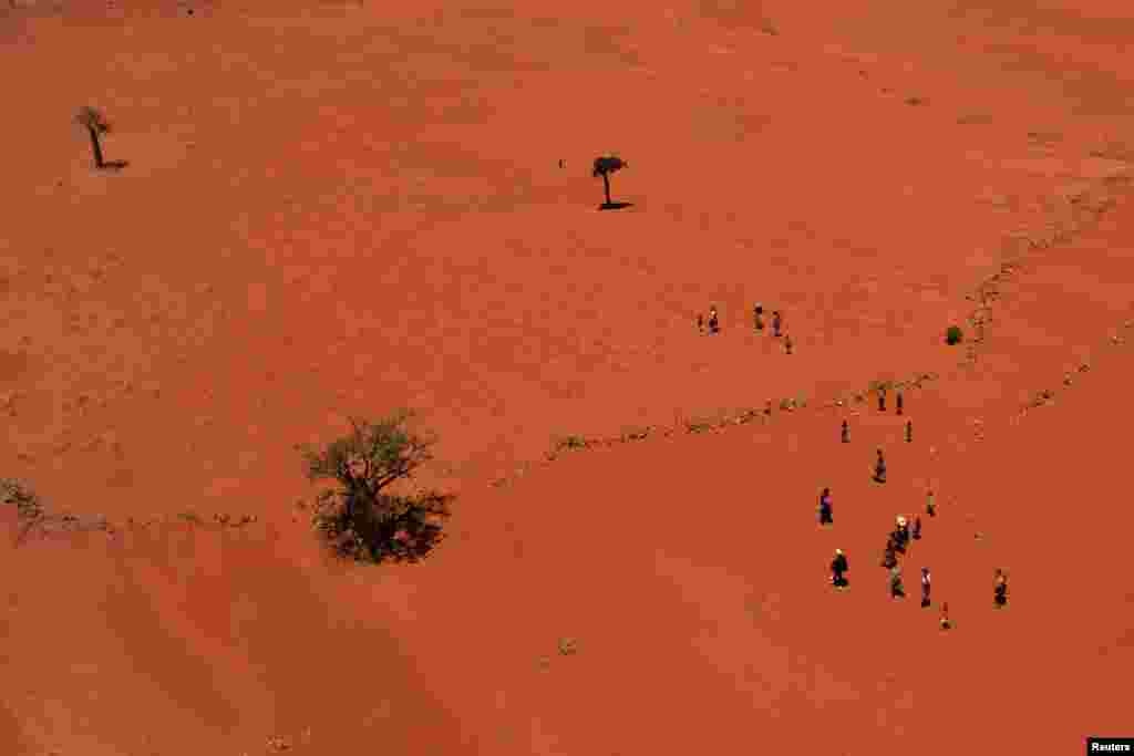 Locals walk across a field covered with red sand in the Anjeky Beanatara, Androy region of Madagascar.
