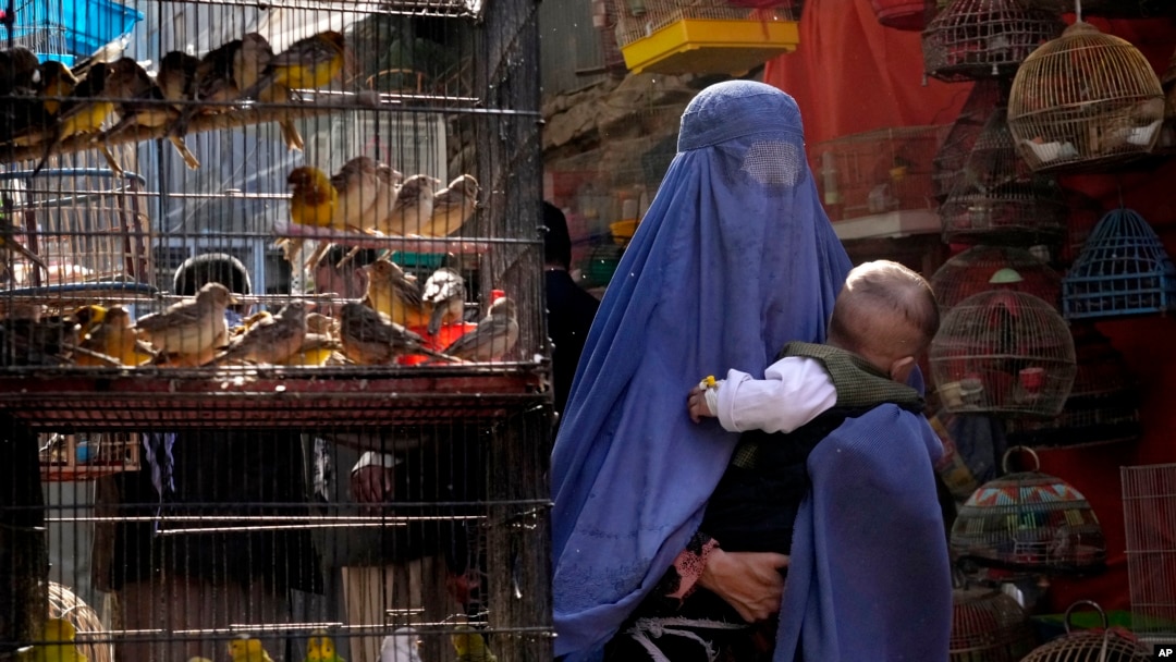 A woman wearing a burqa walks through a bird market as she holds her child, in downtown Kabul, Afghanistan, Sunday, May 8, 2022. 