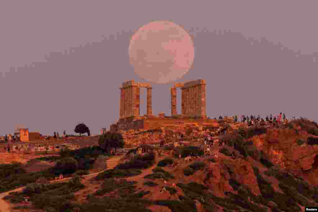 People watch a full moon, known as the "Flower Moon," rising behind the Temple of Poseidon, before a lunar eclipse in Cape Sounion, near Athens, Greece, May 15, 2022.