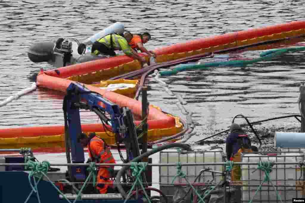 People contain an oil spillage at the scene where a yacht caught fire on May 28, 2022, in Torquay Marina in Torquay, Britain.