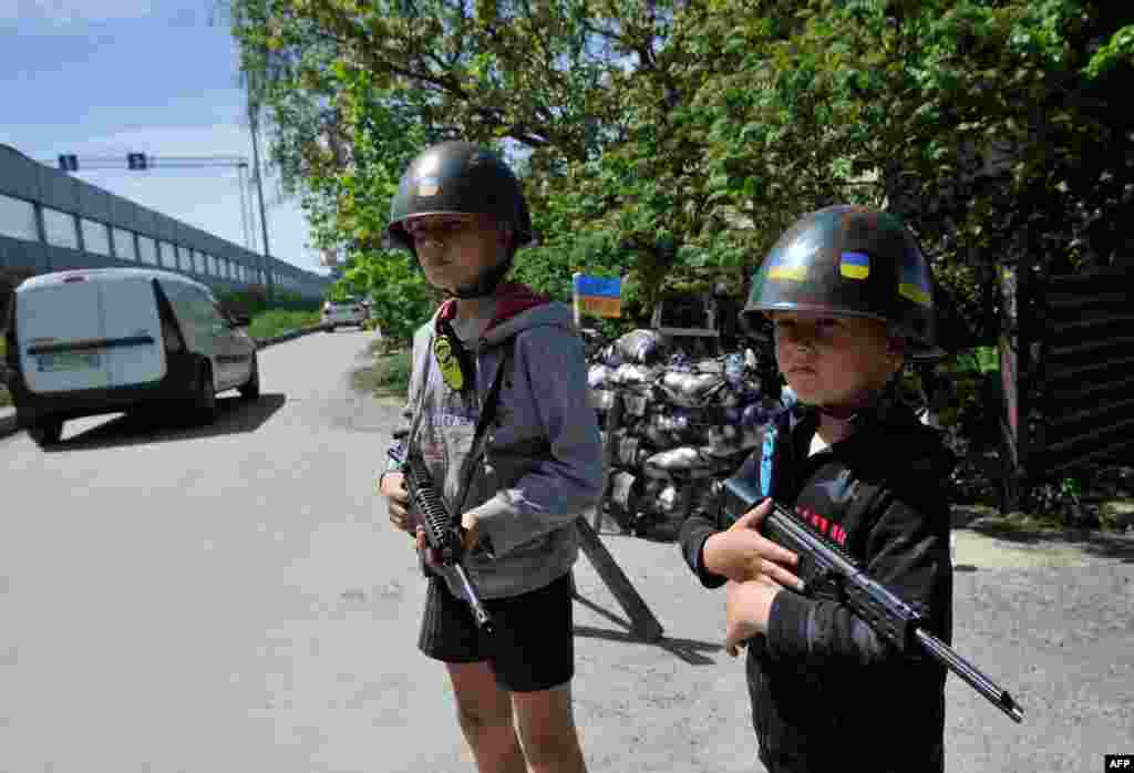 Anak-anak Ukraina bermain sebagai tentara pertahanan teritorial di "pos pemeriksaan" tiruan di desa Stoyanka, wilayah Kyiv, di tengah invasi Rusia ke Ukraina (19/5). (Foto: AFP)