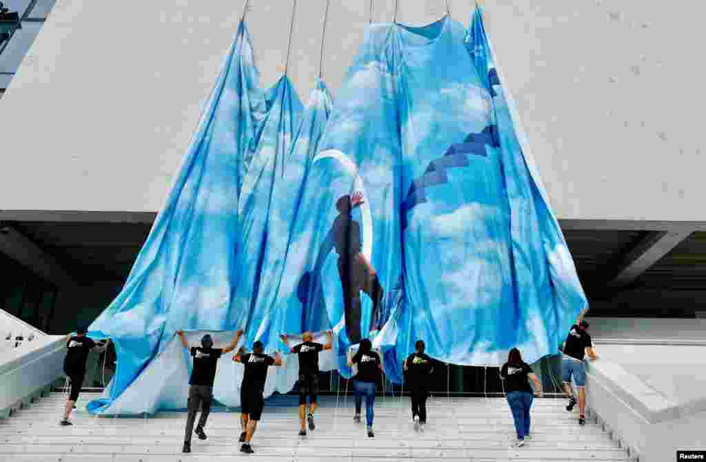 Workers set up a giant canvas of the official poster of the 75th Cannes Film Festival featuring actor Jim Carrey in the film The Truman Show, on the facade of the festival palace ahead of the opening ceremony in Cannes, France.