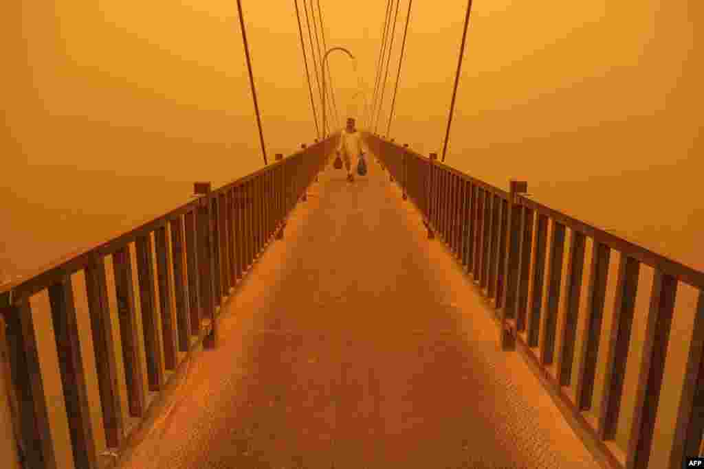 A man walks on a pedestrian bridge along the Euphrates river in the city of Nasiriyah in Iraq's southern Dhi Qar province, amidst a heavy dust storm.