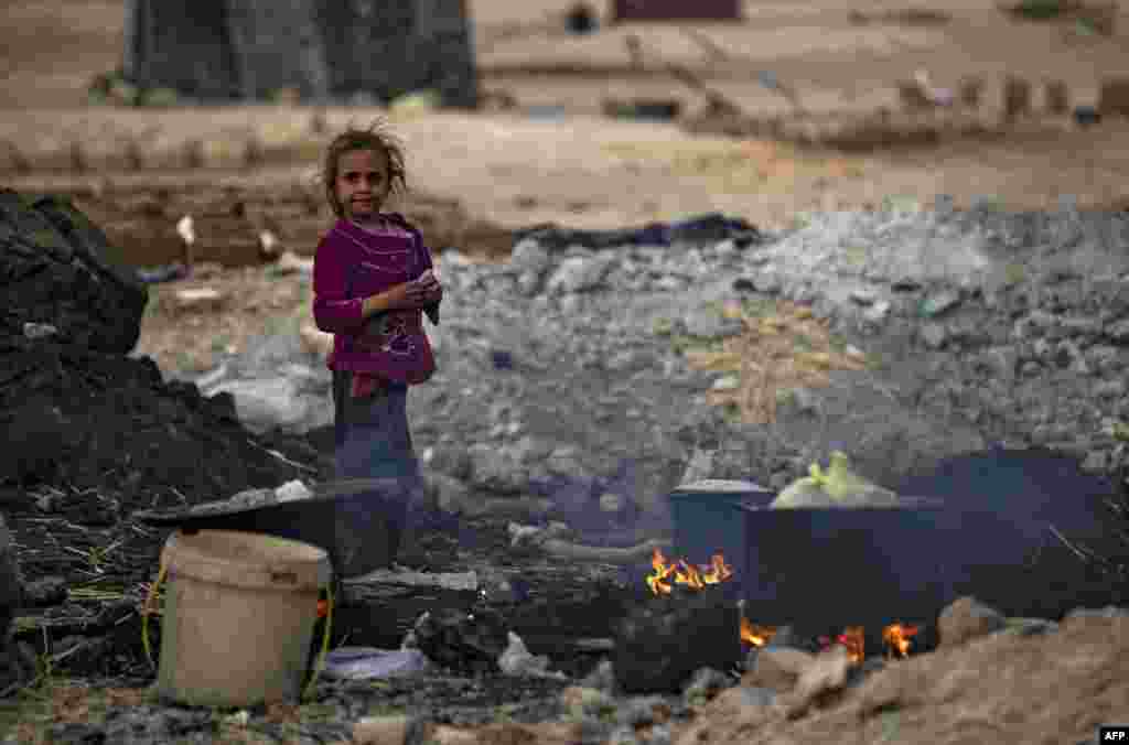 A Syrian girl stands near cooking pots placed on fire amidst the remains of asphalt at the Sahlah al-Banat camp for displaced people in the countryside of Raqa in northern Syria, Nov. 7, 2022.