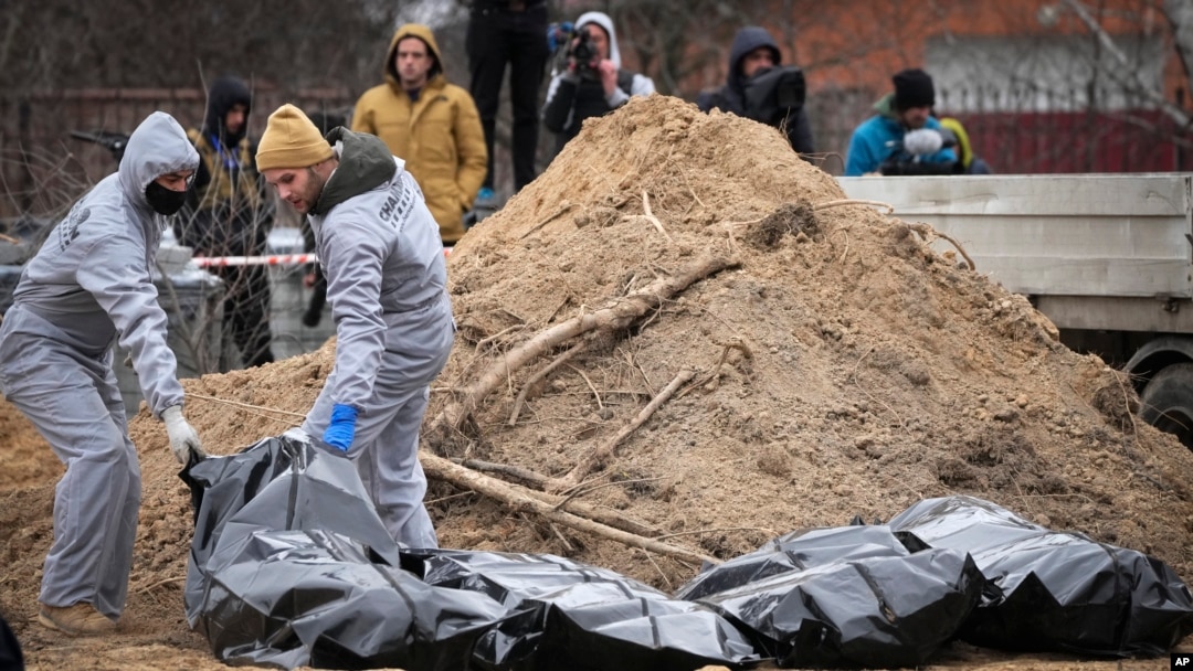 FILE - Men wearing protective gear exhume bodies of some of the civilians killed during the Russian occupation of Bucha, on the outskirts of Kyiv, Ukraine, April 13, 2022.