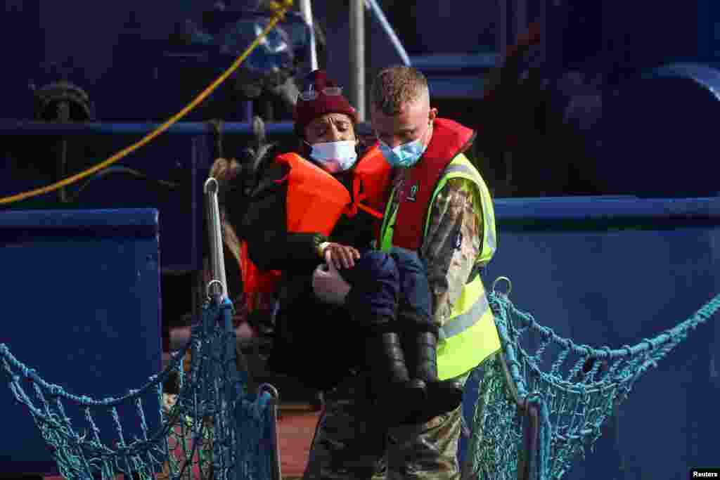A member of the British military assists a migrant woman arriving at Britain's Port of Dover after being rescued while crossing the English Channel.