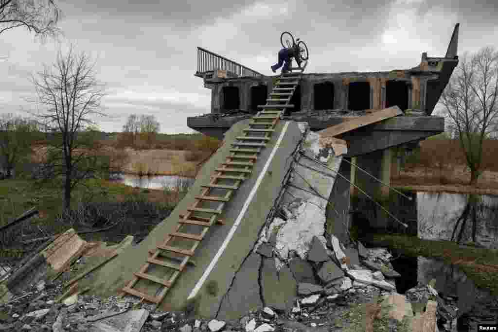 A local resident Mykola, 70, climbs down with a bicycle from a bridge destroyed during Russia's invasion in the village of Kukhari in Kyiv region, Ukraine, April 19, 2022.