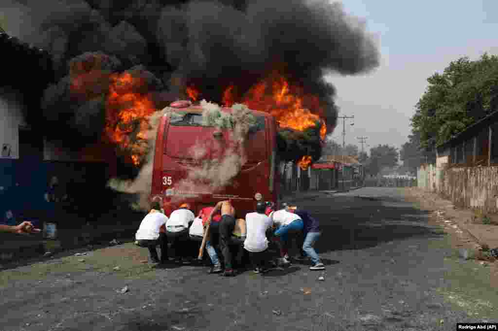 Demonstrators push a bus that was torched during clashes with the Bolivarian National Guard in Urena, Venezuela, near the border with Colombia, Feb. 23, 2019. Venezuela's National Guard fired tear gas on residents clearing a barricaded border bridge between Venezuela and Colombia, heightening tensions over blocked humanitarian aid that opposition leader Juan Guaido has vowed to bring into the country over objections from President Nicolas Maduro.