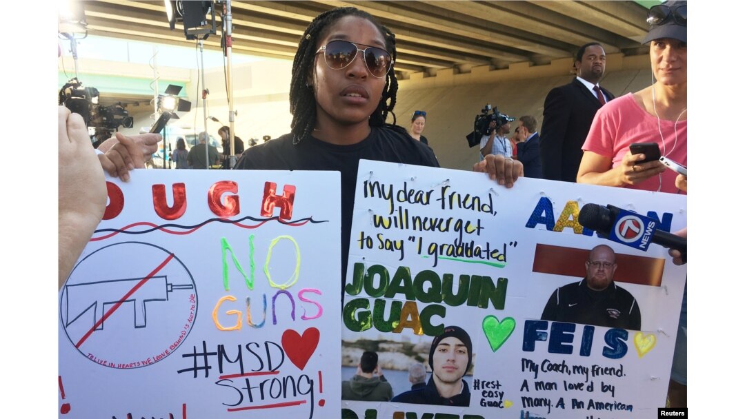 Tyra Hemans, a 19-year-old senior at Marjory Stoneman Douglas High School, sobs as she holds signs honoring slain teachers and friends near the police cordon around the school in Parkland Florida, Feb. 15, 2018.