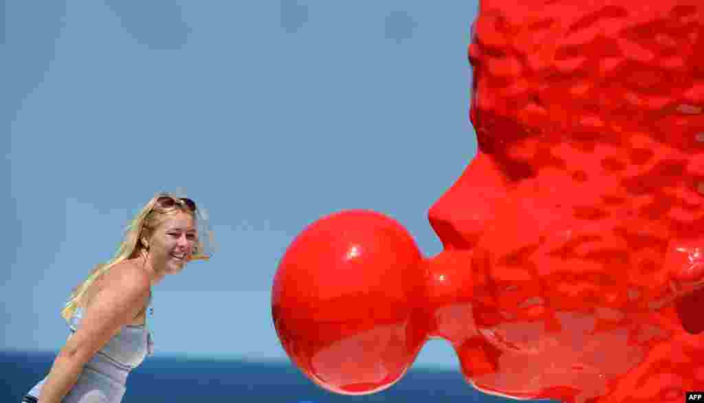A tourist poses next to a two-meter-high blood red sculpture of a head blowing bubble gum by Qian Sihua, which is part of the Sculpture by the Sea exhibition which runs on the Bondi to Tamarama coastal walk in Sydney, Australia.
