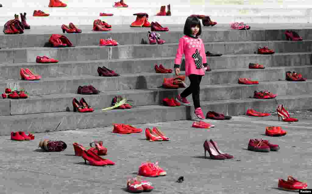 A young girl looks on near an installation of women's red shoes displayed on a staircase, as a symbol to denounce violence against women, in Tirana, Albania, March 8, 2022.
