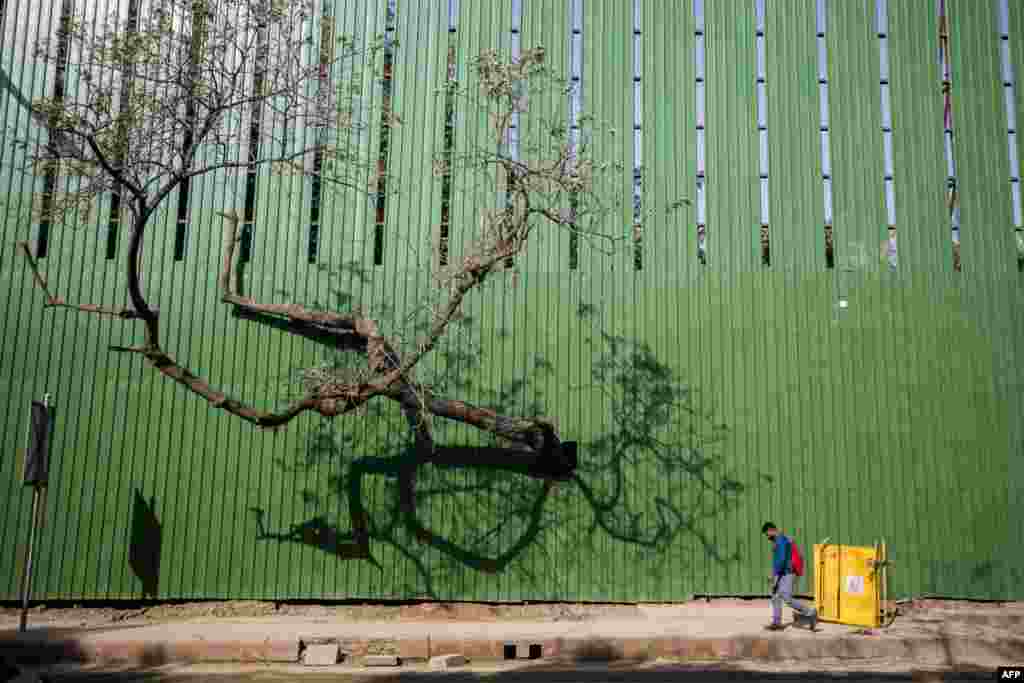 A man walks past the fence of a construction site along a street in New Delhi, India.