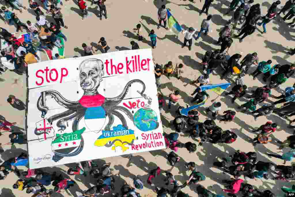 Protesters raise a giant sign depicting Russia's President Vladimir Putin as an octopus with its arms wrapping around the countries of Georgia, Syria and Ukraine, as well as the world globe, during a demonstration in the city of Binnish in Syria's northwestern rebel-held Idlib province.