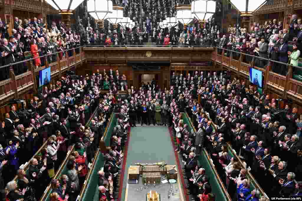 Ukrainian President Volodymyr Zelenskyy, on the screen, receives a standing ovation after he addresses British lawmakers by video link in the House of Commons in London. The Ukrainian leader urged Britain to increase sanctions on Russia, to recognize Russia as “a terrorist country” and to keep Ukraine’s skies safe.
