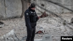 在基輔一處被俄羅斯無人機破壞的建築附近，一名警察站在無人機殘骸邊。(2022年12月14日)