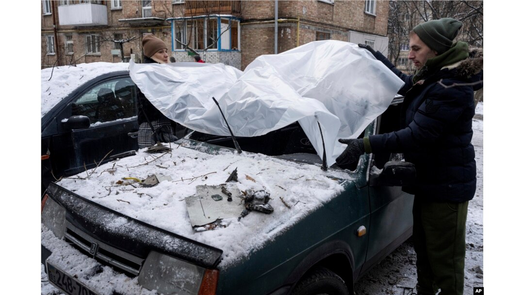 A couple cover their damaged car with a plastic tarp after a Russian attack in Kyiv, Ukraine, Wednesday, Dec. 14, 2022. (AP Photo/Evgeniy Maloletka)