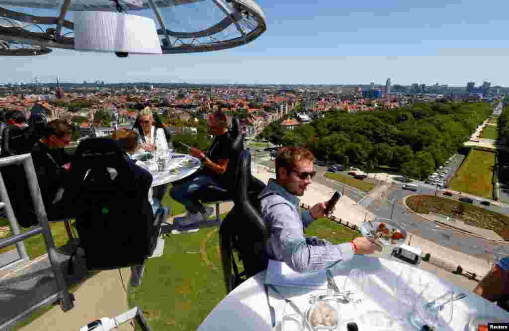 People sit at one of the eight tables on a nine-ton structure, suspended from a crane at a height of 50 meters, that can accommodate a total of thirty two guests for a meal during an event known as "Dinner in the Sky" outside Koekelberg Basilica in Brussels, Belgium.