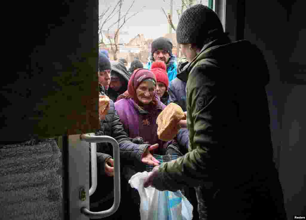 Local residents receive bread during the distribution of humanitarian aid in the besieged southern port city of Mariupol amid the ongoing Russian invasion of Ukraine, April 4, 2022.