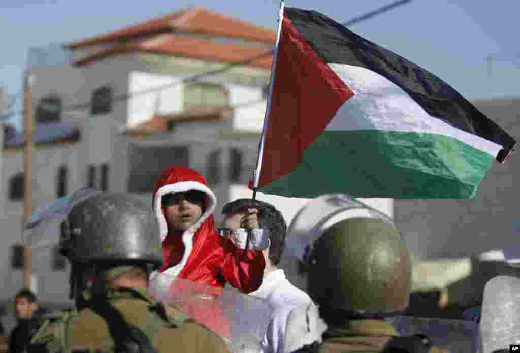 A Palestinian child dressed as Santa Claus holds a Palestinian flag while standing in front of Israeli border police during a demonstration against Israel's separation barrier in the West Bank village of Al-Masara, near Bethlehem.