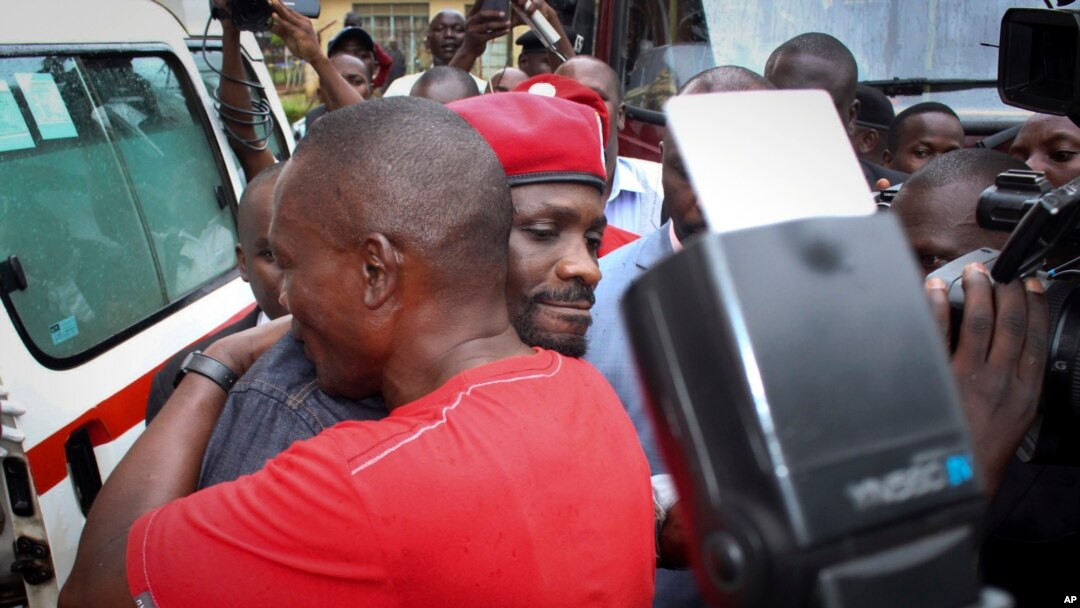 Ugandan pop star Kyagulanyi Ssentamu, better known as Bobi Wine, center, wears a beret and is hugged by a supporter as he gets into an ambulance after leaving the courthouse in Gulu, Uganda, Aug. 27, 2018. 