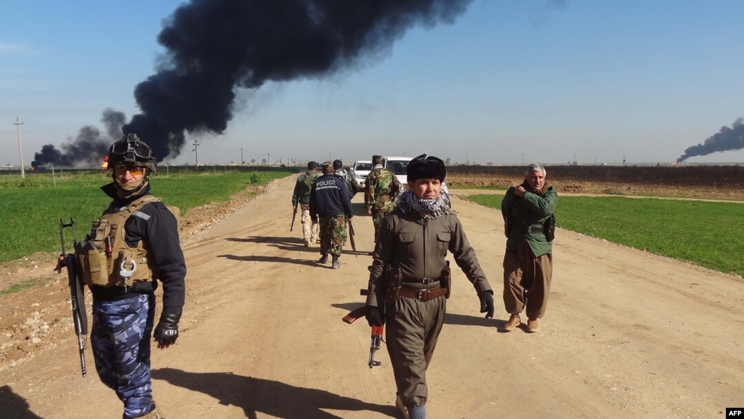 FILE - Members of the Kurdish Peshmerga forces and the Iraqi security forces patrol on a road as smoke billows from the Khubbaz oil field, some 25 km west of the northern city of Kirkuk, Feb. 2, 2015. 