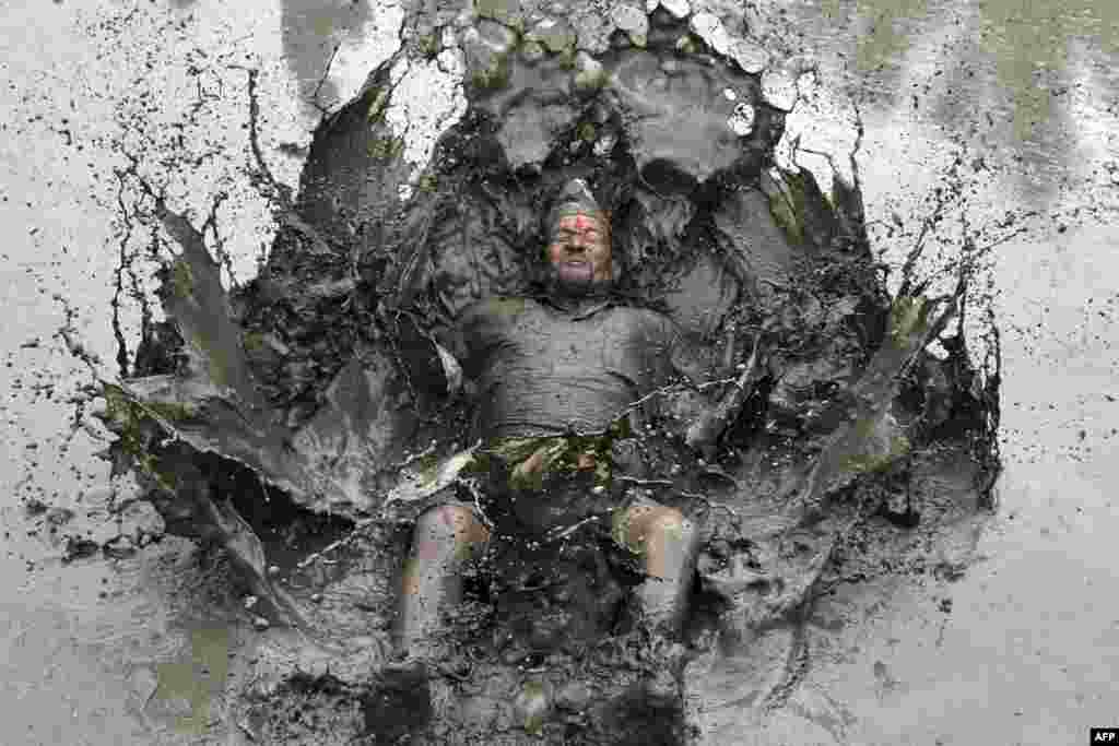 A mud-covered farmer plays in a rice paddy field during "National Paddy Day," which marks the start of the annual rice planting season, in Tokha village on the outskirts of Kathmandu, Nepal.