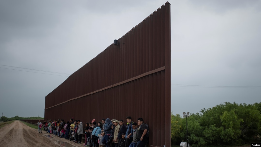 Solicitantes de asilo procedentes de Centroamérica esperan en el muro fronterizo entre México y EE.UU., en Penitas, Texas para entregarse a la patrulla. Abril 2 de 2019.