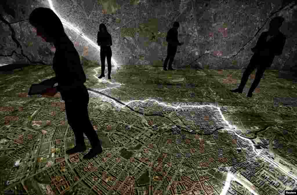 Museum staff walk with mobile devices over a giant illuminated aerial photograph of Berlin, including the marked course of the Berlin Wall and places related to the former East German Ministry for State Security (MfS), known as the Stasi, at the exhibition 'The Stasi in Berlin' inside former Stasi prison, Hohenschoenhausen, Berlin. 