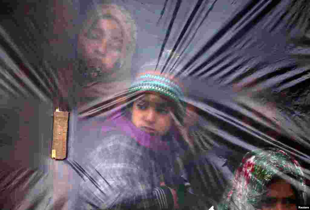 Children look out from a window, covered with a plastic sheet to protect from cold, on a winter day in a village of south Kashmir's Pulwama district, India.