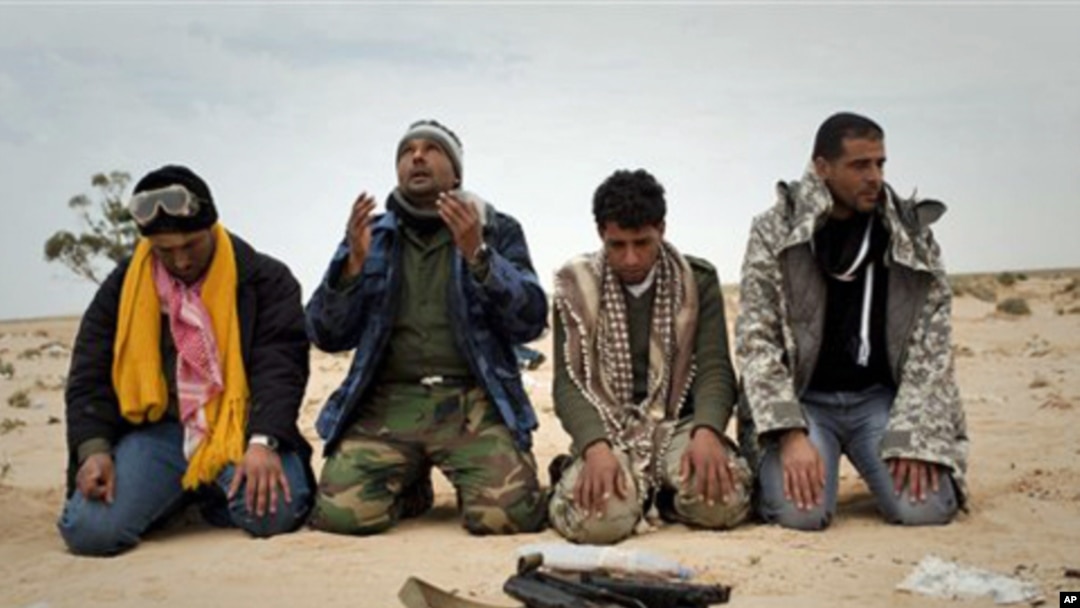 Libyan rebels pray in the desert in front a weapon on the frontline near Sultan, south of Benghazi, March 18, 2011