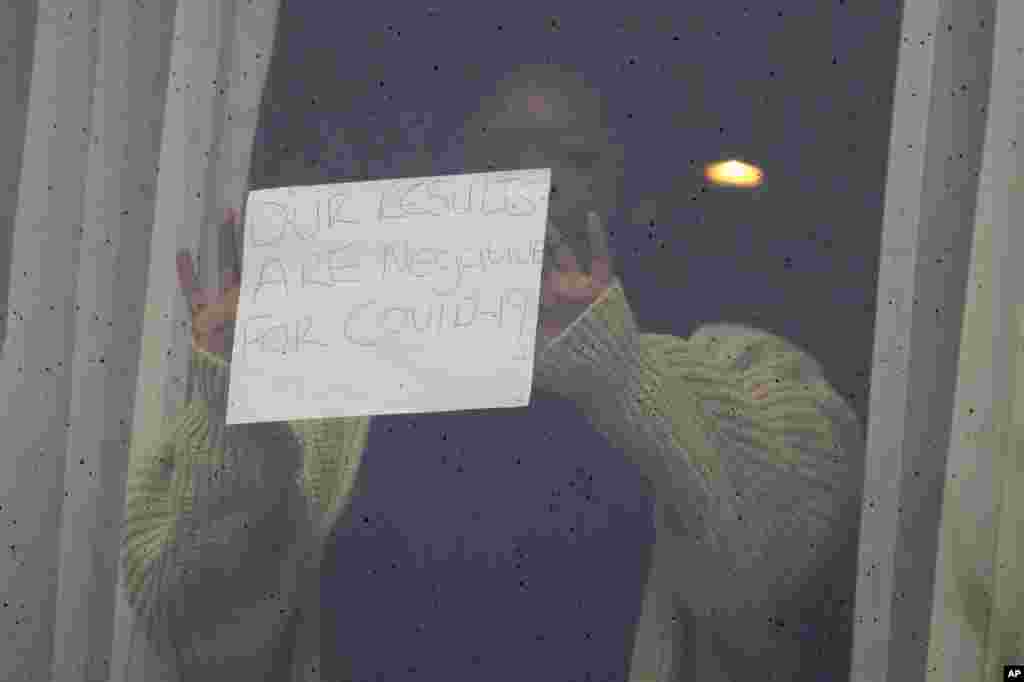 A woman holds up a sign for the media against the window at the Radisson Blu Edwardian Hotel, near London's Heathrow Airport, where passengers will remain during a 10-day quarantine period after arriving in England at the airport.