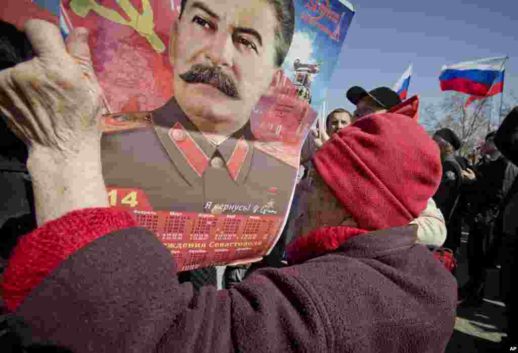 An elderly woman holds a calendar depicting Soviet leader Josef Stalin while watching a broadcast of Russian President Vladimir Putin's speech on Crimea, as thousands of pro-Russian people gathered to watch the address, in Sevastopol, Crimea, Ukraine, March 18, 2014.