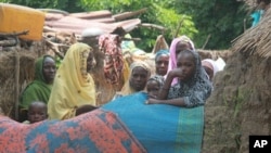Women and children stand outside their houses following the visit of government officials to the mosque that was attacked by gunmen in Konduga, Maiduguri, Nigeria, Aug, 13, 2013.