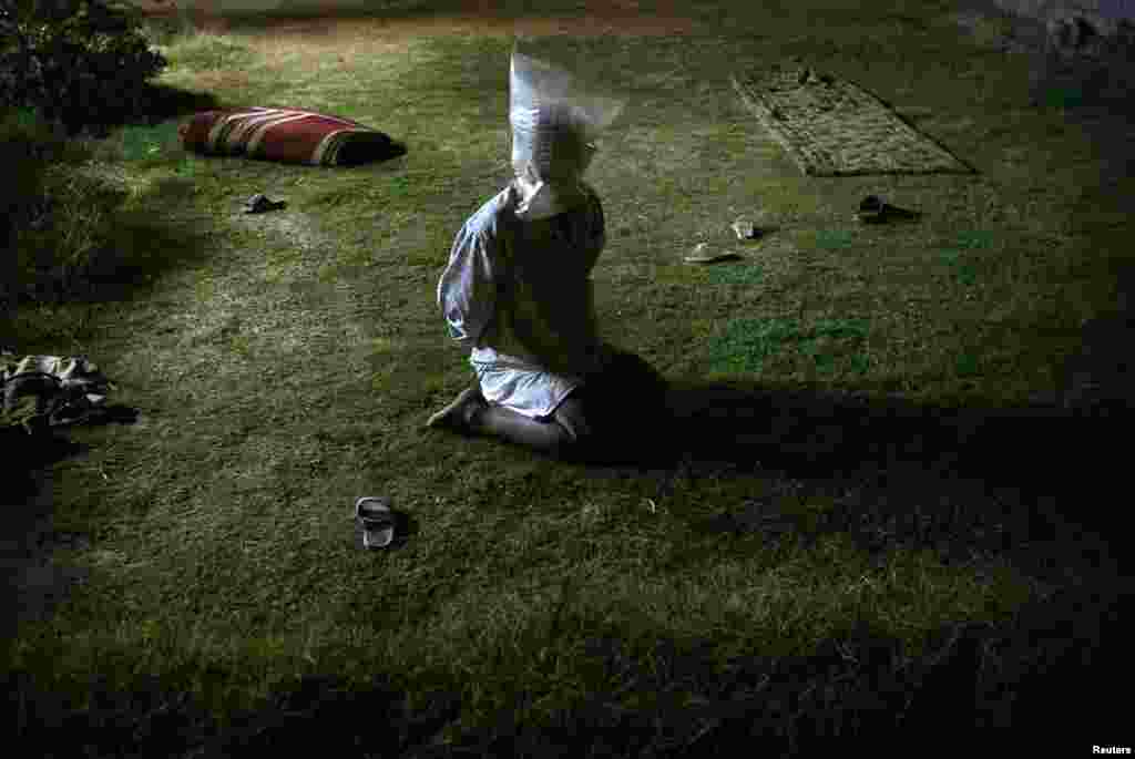 A detained Iraqi man with a plastic bag covering his head sits in garden of a house searched by U.S. soldiers during a night raid in Tikrit, Oct. 30, 2003.