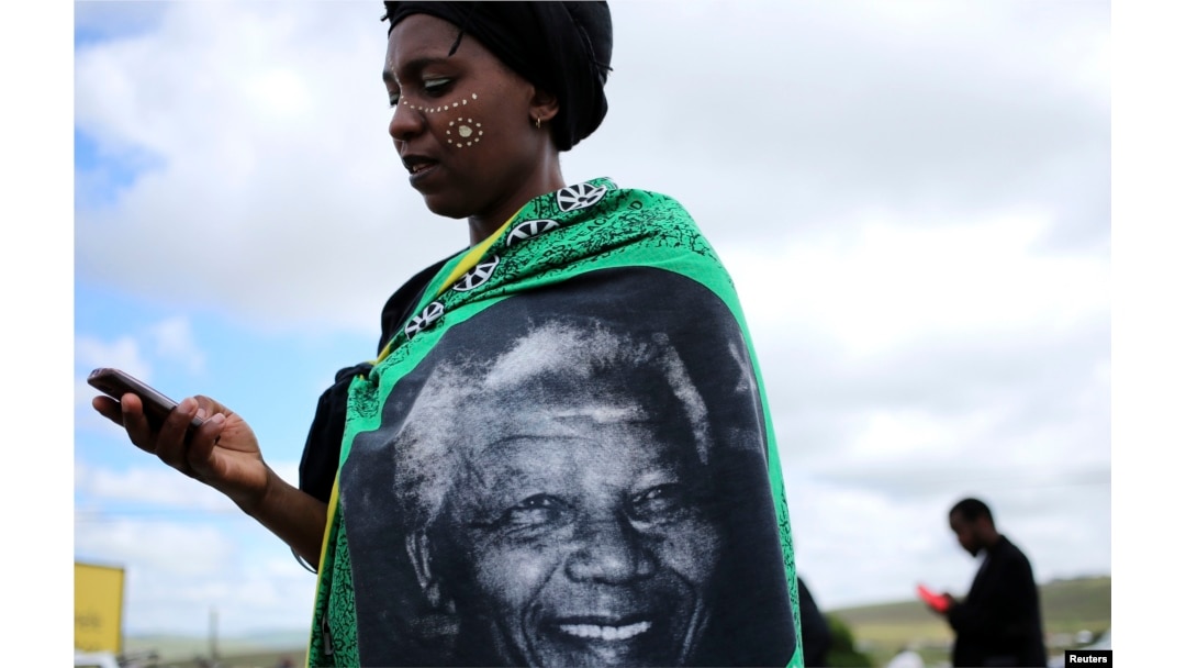 A woman, draped in a cloth with an image of former South African President Nelson Mandela, uses a mobile phone during Mandela's funeral at his ancestral village of Qunu in Eastern Cape province, south of Johannesburg, Dec. 15, 2013.